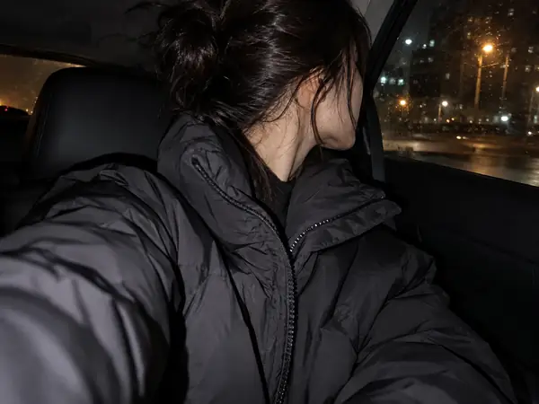A blonde woman taking a close-up night selfie in a dim car with a soft digital-camera flash